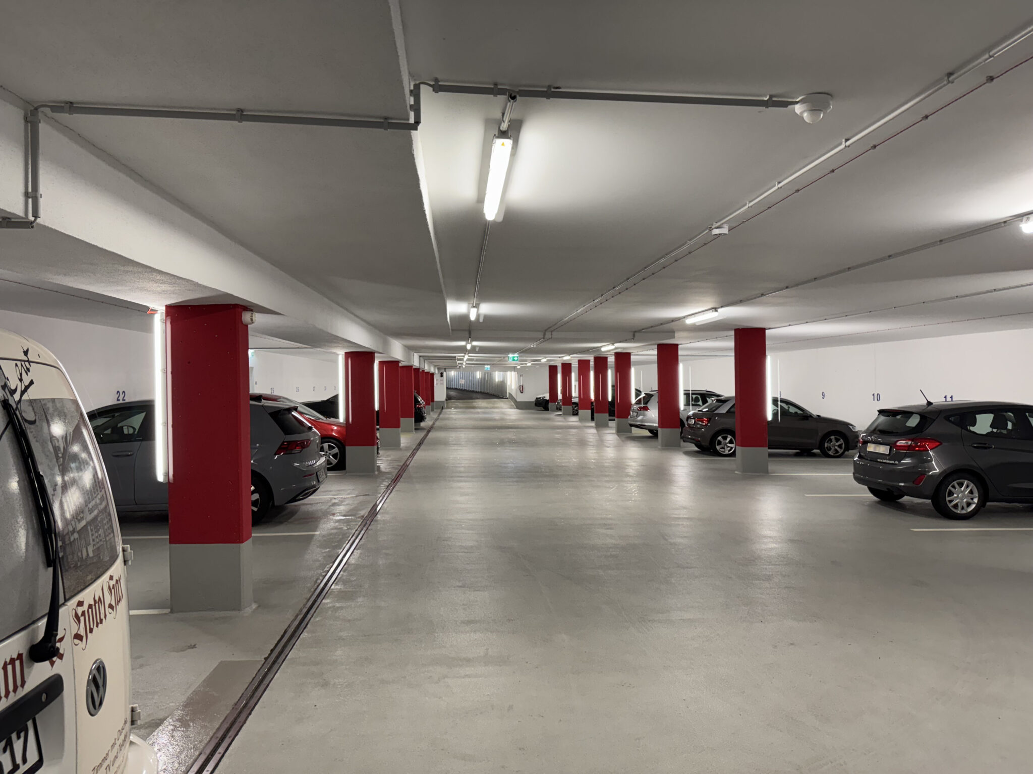 Tiefgarage Hotel INCLUDiO Regensburg Autos parken links und rechts zwischen roten Säulen, die Garage ist gut mit Neonlampen beleuchtet