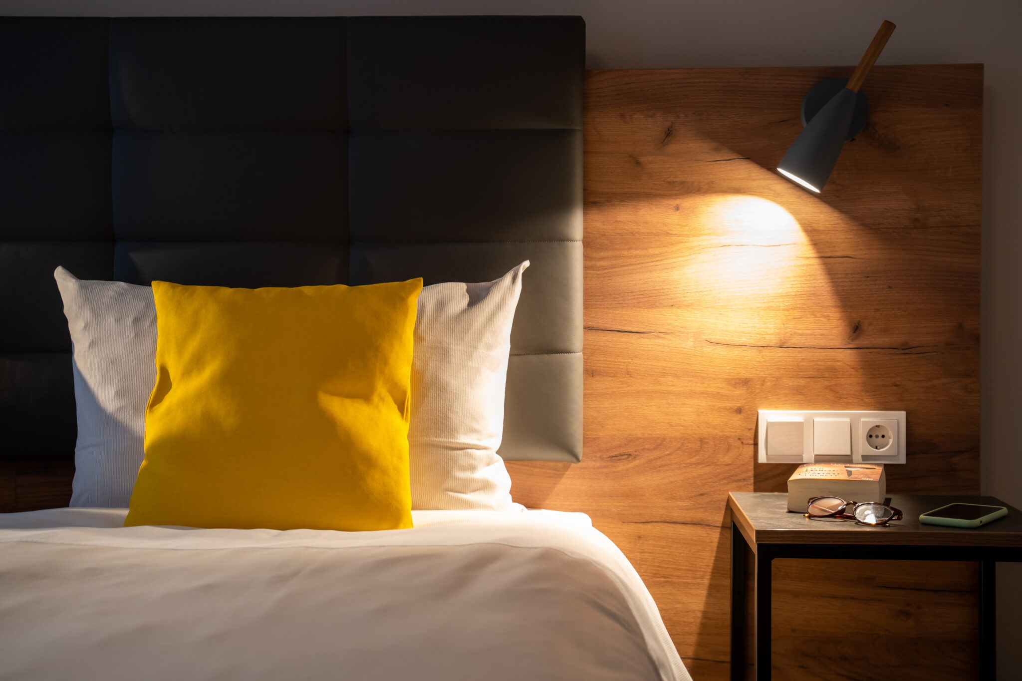 Ein Bett mit einem gelben Kissen und einer modernen Nachttischlampe aus einem Hotelzimmer im Hotel INCLUDiO.