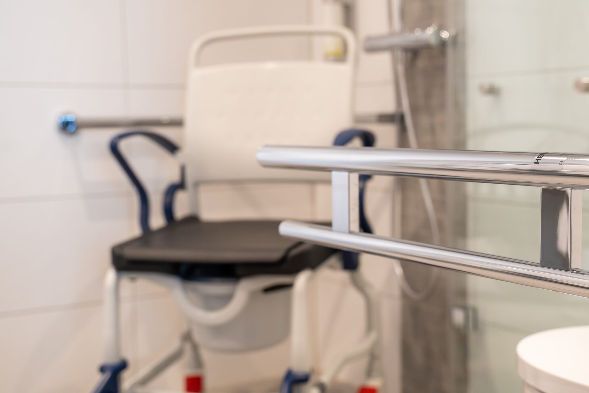 Duschstuhl mit schwarzem Sitz in einem Badezimmer, ausgestattet mit Haltegriffen und Duschbereich.