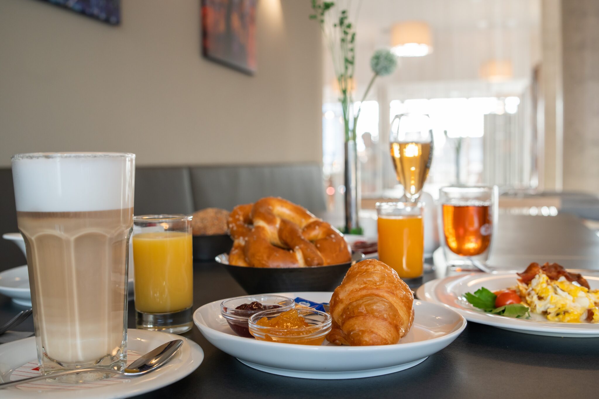 Frühstückstisch mit verschiedenen Speisen, darunter Croissant, Marmelade, Getränke und Brötchen.