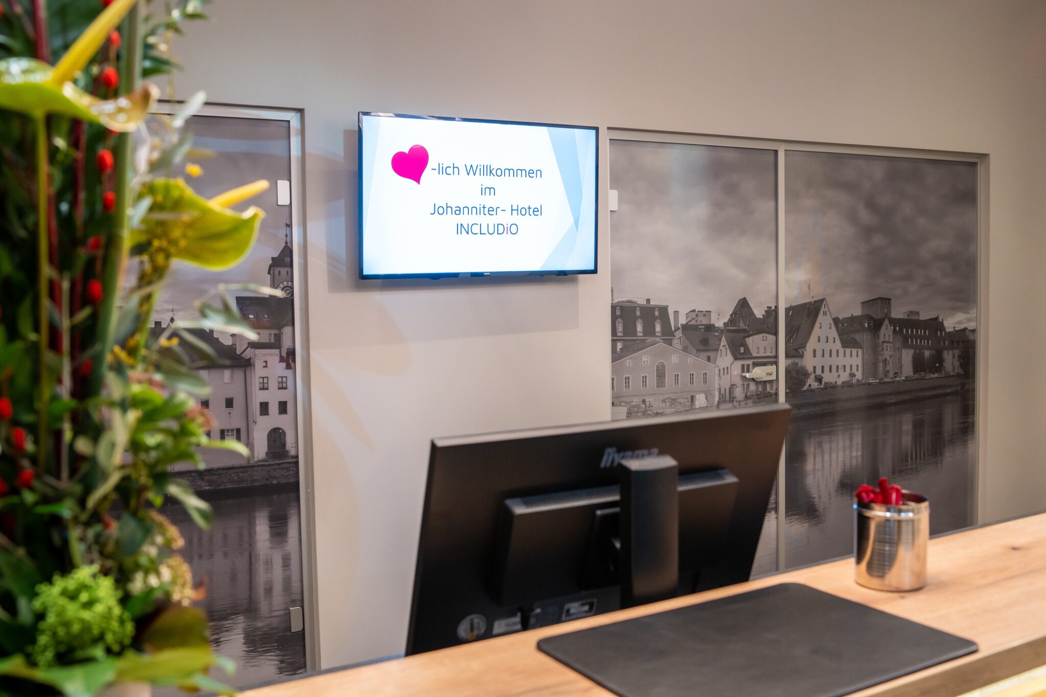 Rezeption mit Bildschirm, der Willkommen im Johanniter-Hotel INCLUDiO anzeigt.