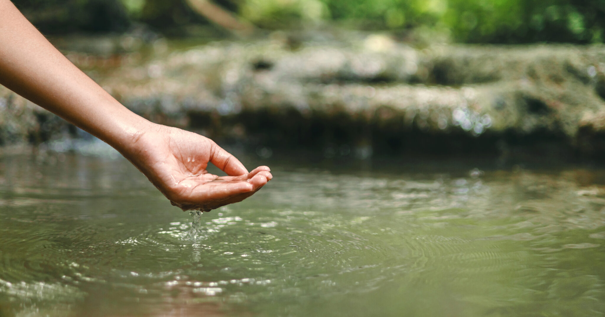 Eine Hand, die in einen ruhigen Gewässer greift, mit Wassertropfen, die abperlen.